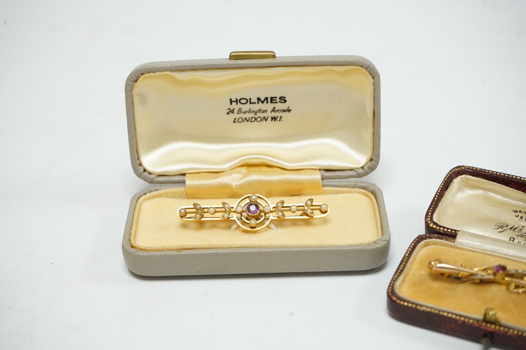 Two bar brooches, early 20th century, comprising: one set with a circular-cut garnet, accented by seed pearls, mounted in 9ct gold, length 4.4cm, British hallmarks; and another set with a circular-cut amethyst and seed p